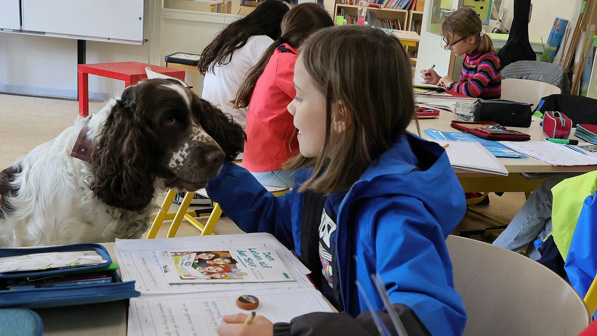 Schülerin Matilda macht eine Schreibaufgabe, Hund Linn sitzt neben ihr.