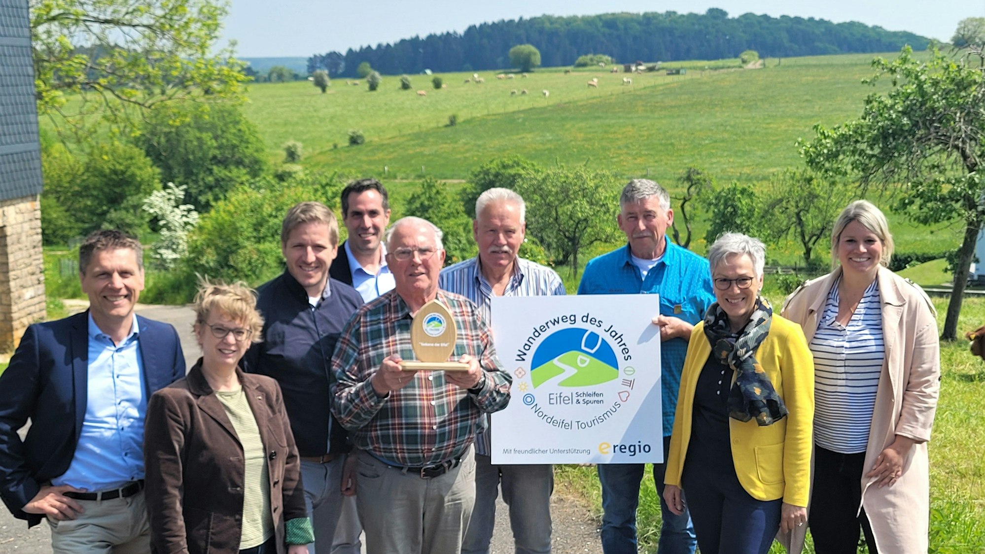 Das Bild zeigt eine Gruppe von Personen vor einer grünen Wiese. Drei Männer halten die Auszeichnungen, die ihnen verliehen wurden.