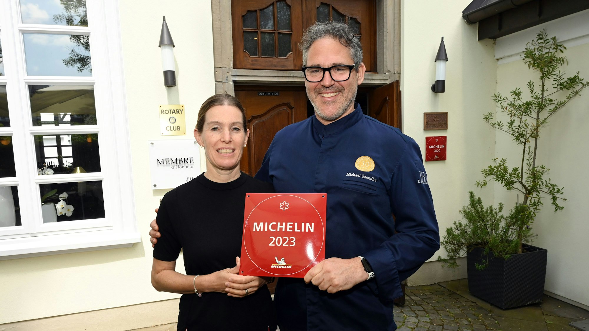 Ein Koch und seine Frau stehen nebeneinander und halten die Auszeichnung „Michelin 2023“ in den Händen.