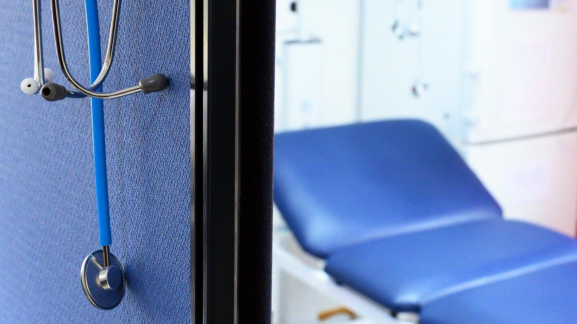 Stethoskope hängen im Behandlungszimmer einer Hausarztpraxis über einer Trennwand.