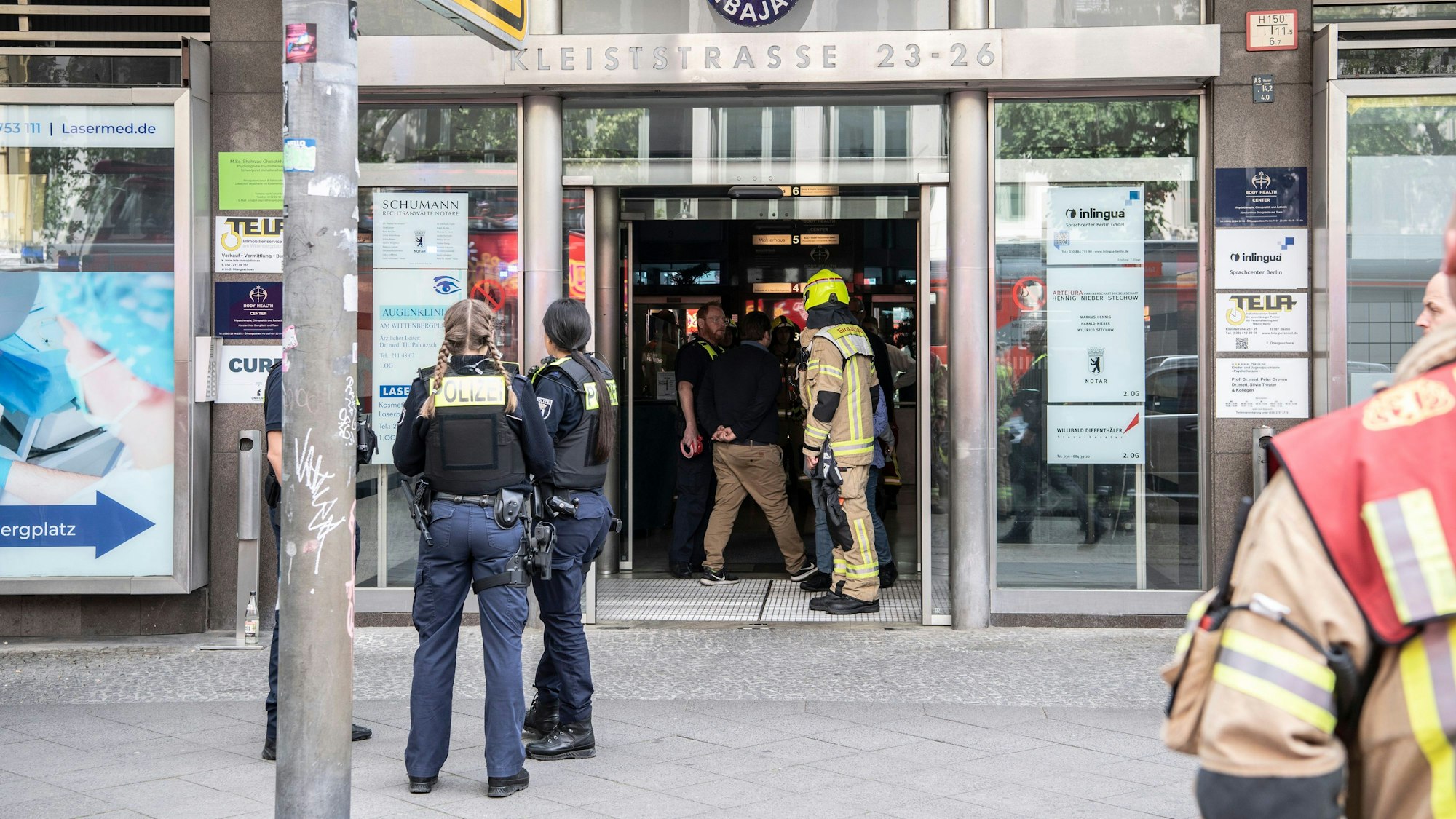 Einsatzkräfte der Feuerwehr und Polizei stehen in einem Hauseingang in Berlin. In dem mehrgeschossigen Gebäude kam es zu einem tödlichen Unfall mit einem Paternoster.