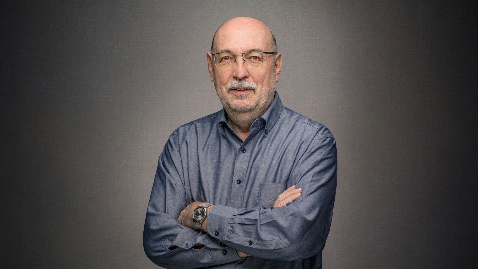 Jürgen Schmidt steht vor einem grauen Hintergrund und verschränkt die Arme.