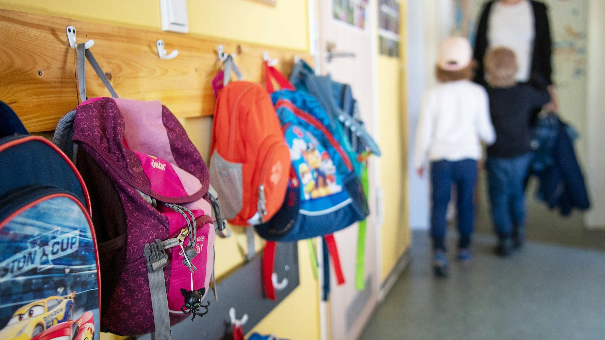 Das Foto zeigt die Garderobe in einer Kita. An den Haken hängen bunte Rucksäcke.