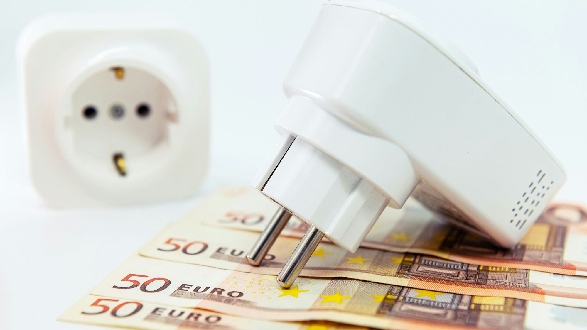 Ein Zwischenstecker liegt auf vier 50-Euro-Scheinen, im Hintergrund ist eine herkömmliche Steckdose zu sehen.