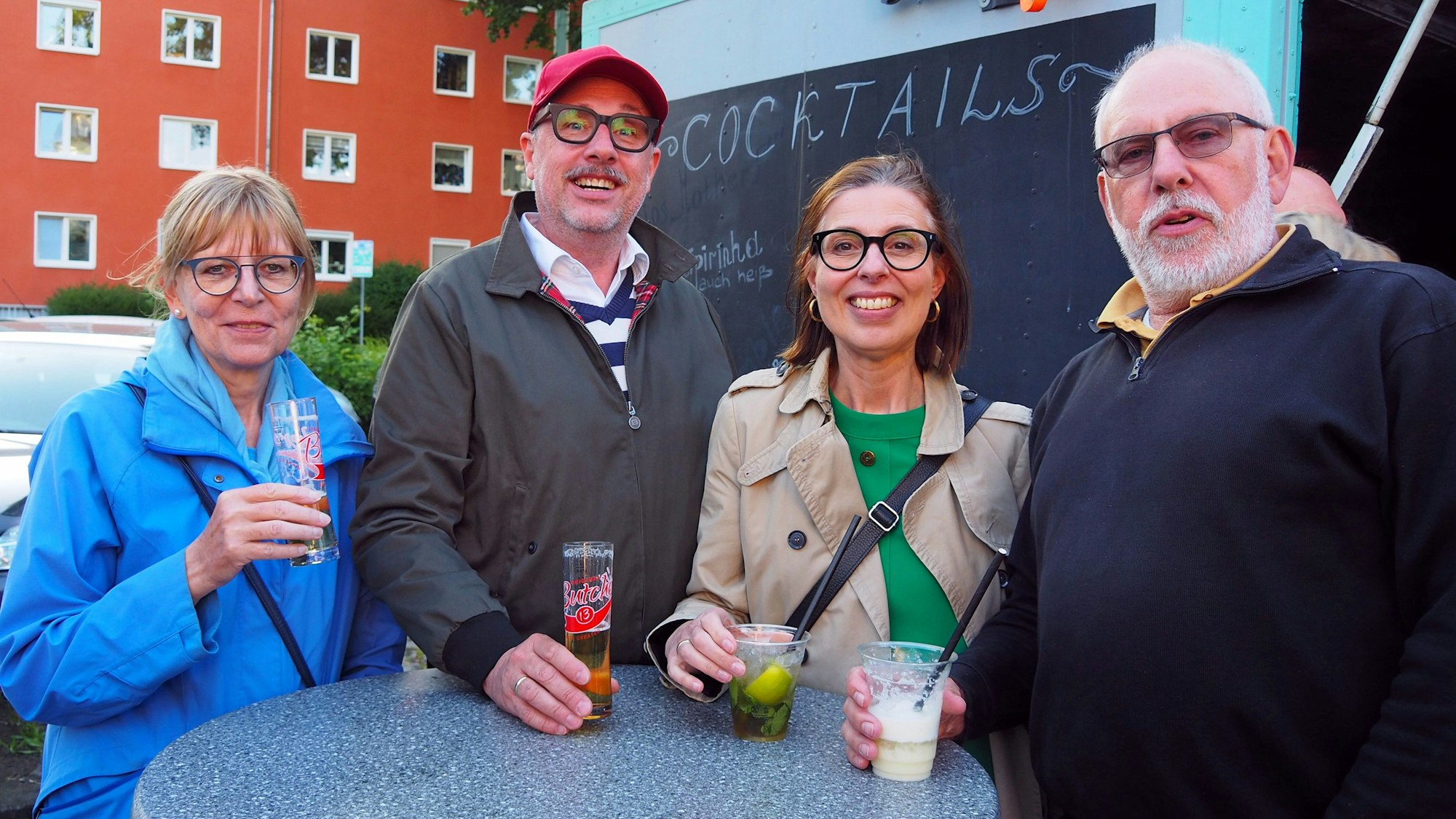Zwei Paare im mittleren Alter stehen um einen Stehtisch, zwei haben Kölsch, zwei Cocktails in der Hand.