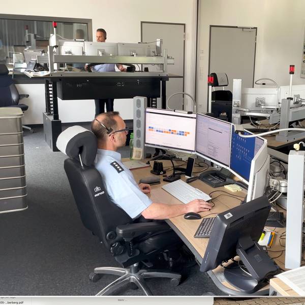 Ein Polizist in Uniform sitzt an einem Computerarbeitsplatz vor vier Bildschirmen.