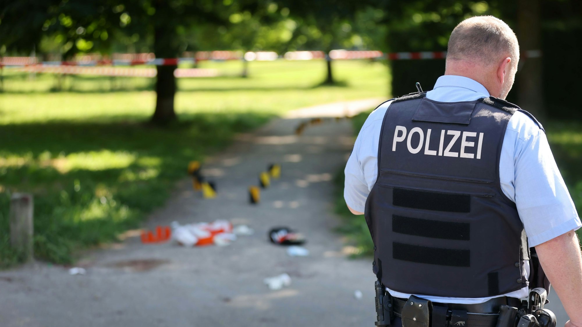 Ein Polizist steht vor einem Park, der mit Absperrband abgesichert wurde.