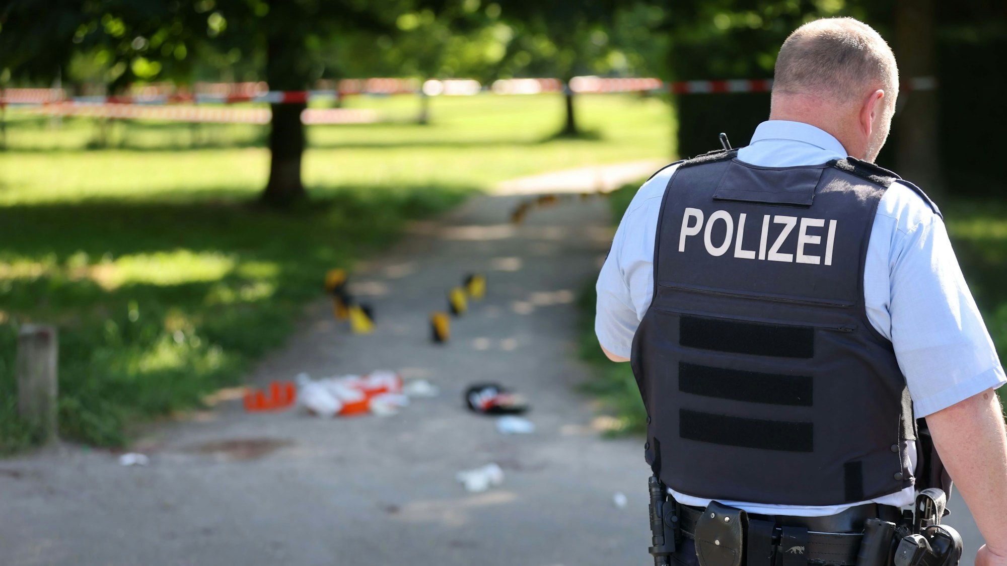 Ein Polizist überwacht den abgesperrten Bereich eines Tatorts - er steht mit dem Rücken zur Kamera.