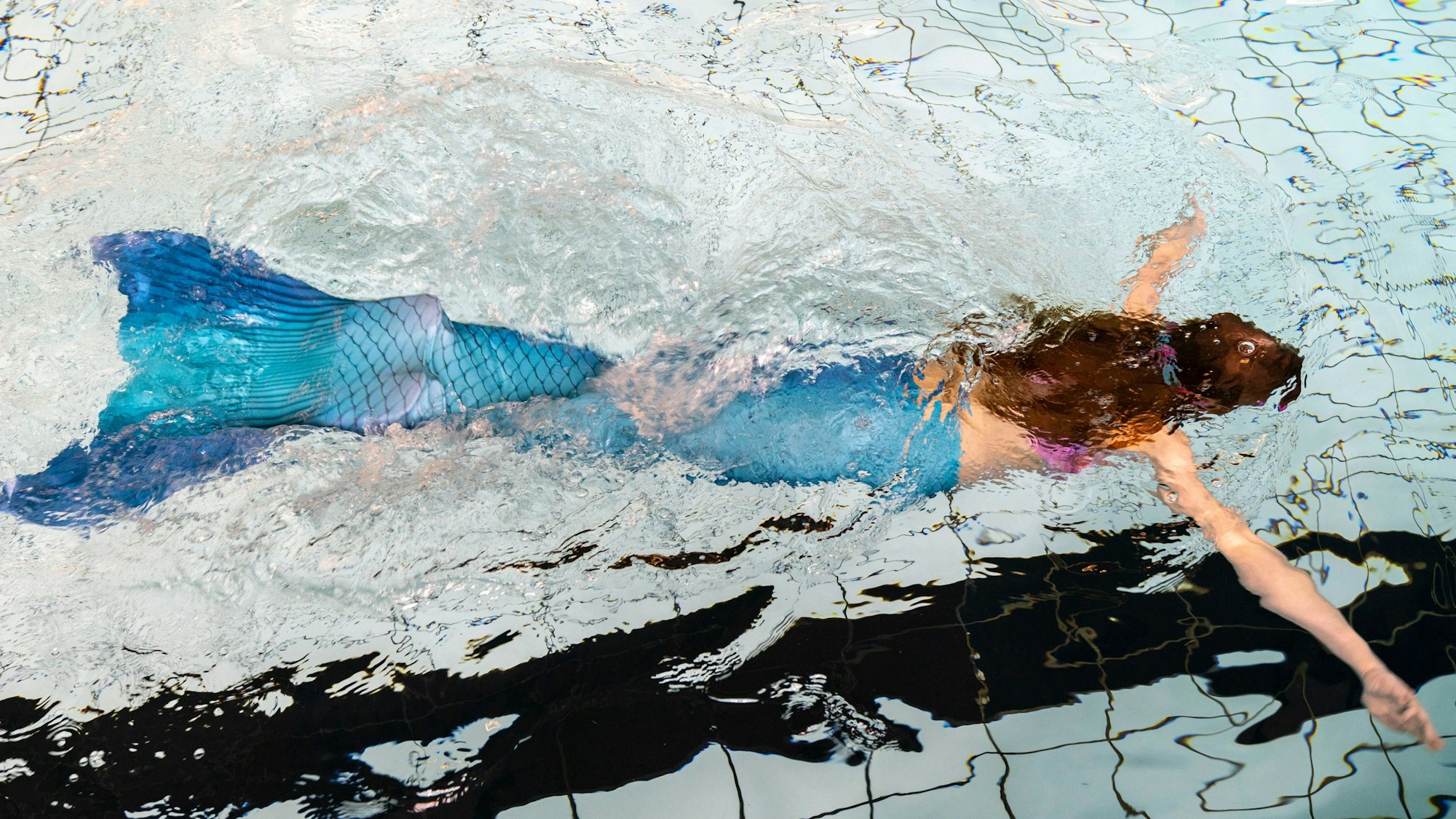 Ein Mädchen schwimmt als Meerjungfrau mit einer Flosse in einem Schwimmbecken eines Hallenbades.