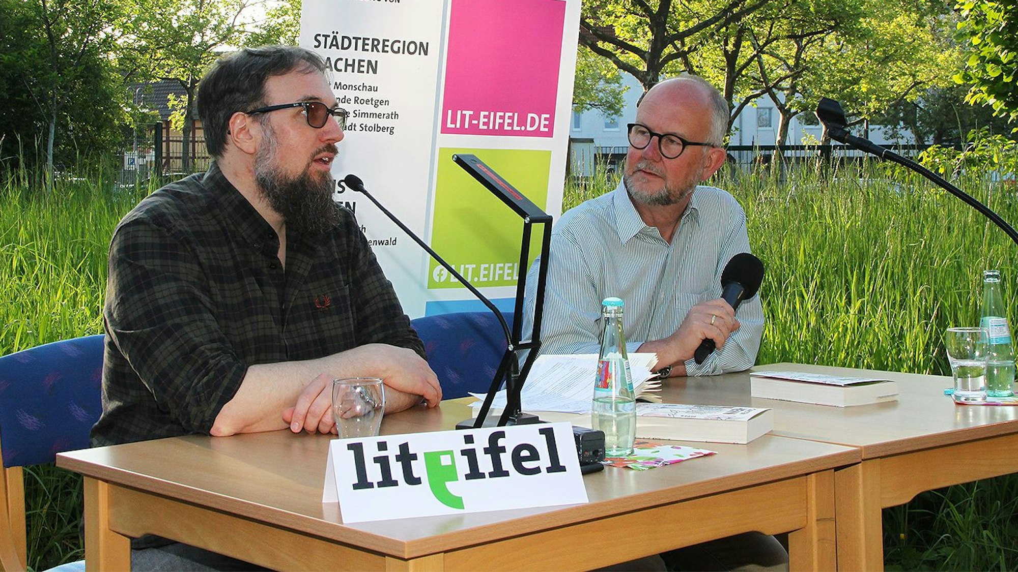 Das Bild zeigt zwei Männer, die an einem Tisch sitzen und sich unterhalten.