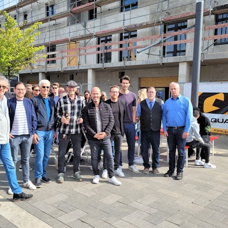Eine Gruppe Menschen steht vor einem Neubau, an dem Richtfest gefeiert wird.