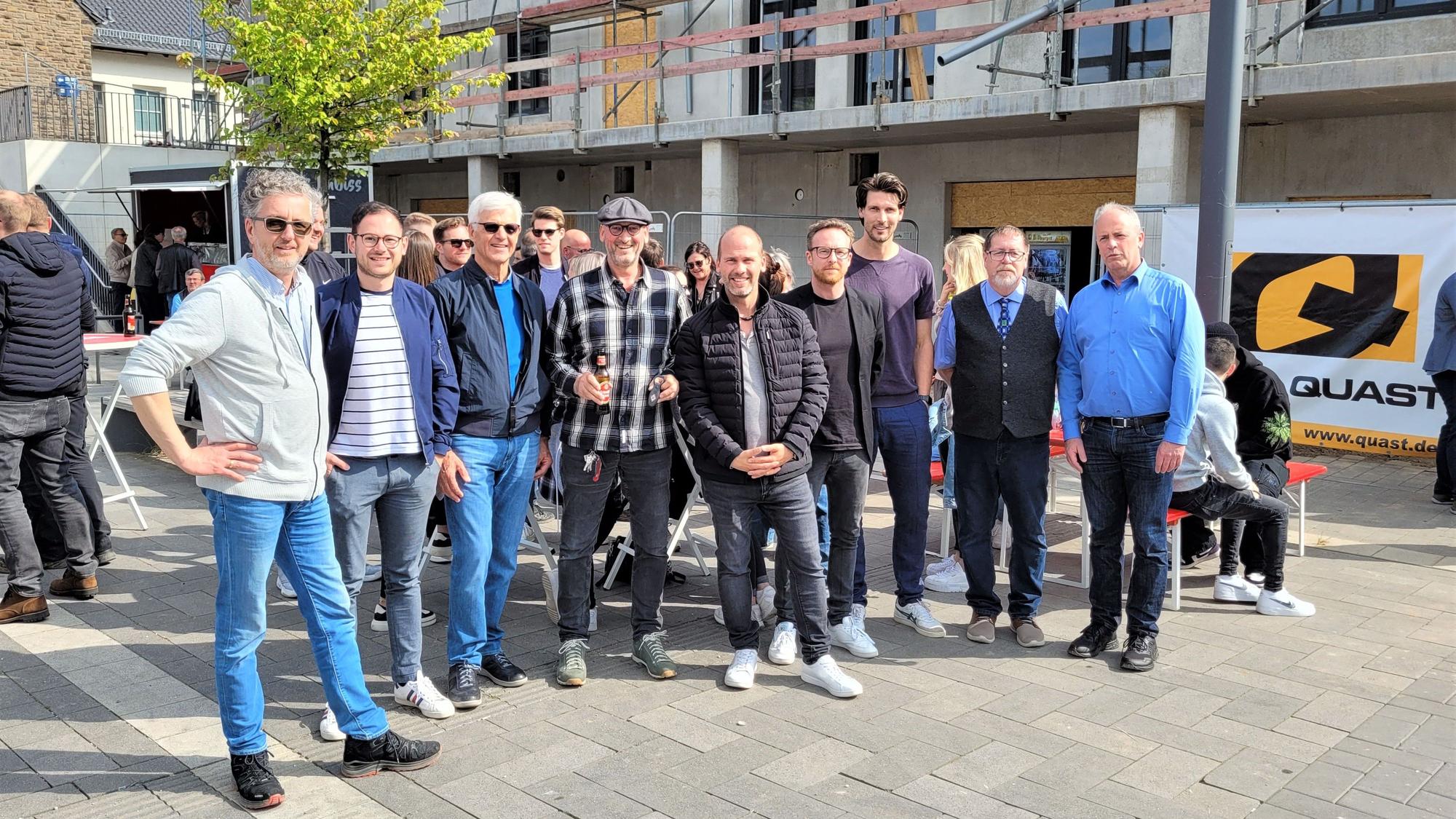 Eine Gruppe Menschen steht vor einem Neubau, an dem Richtfest gefeiert wird.