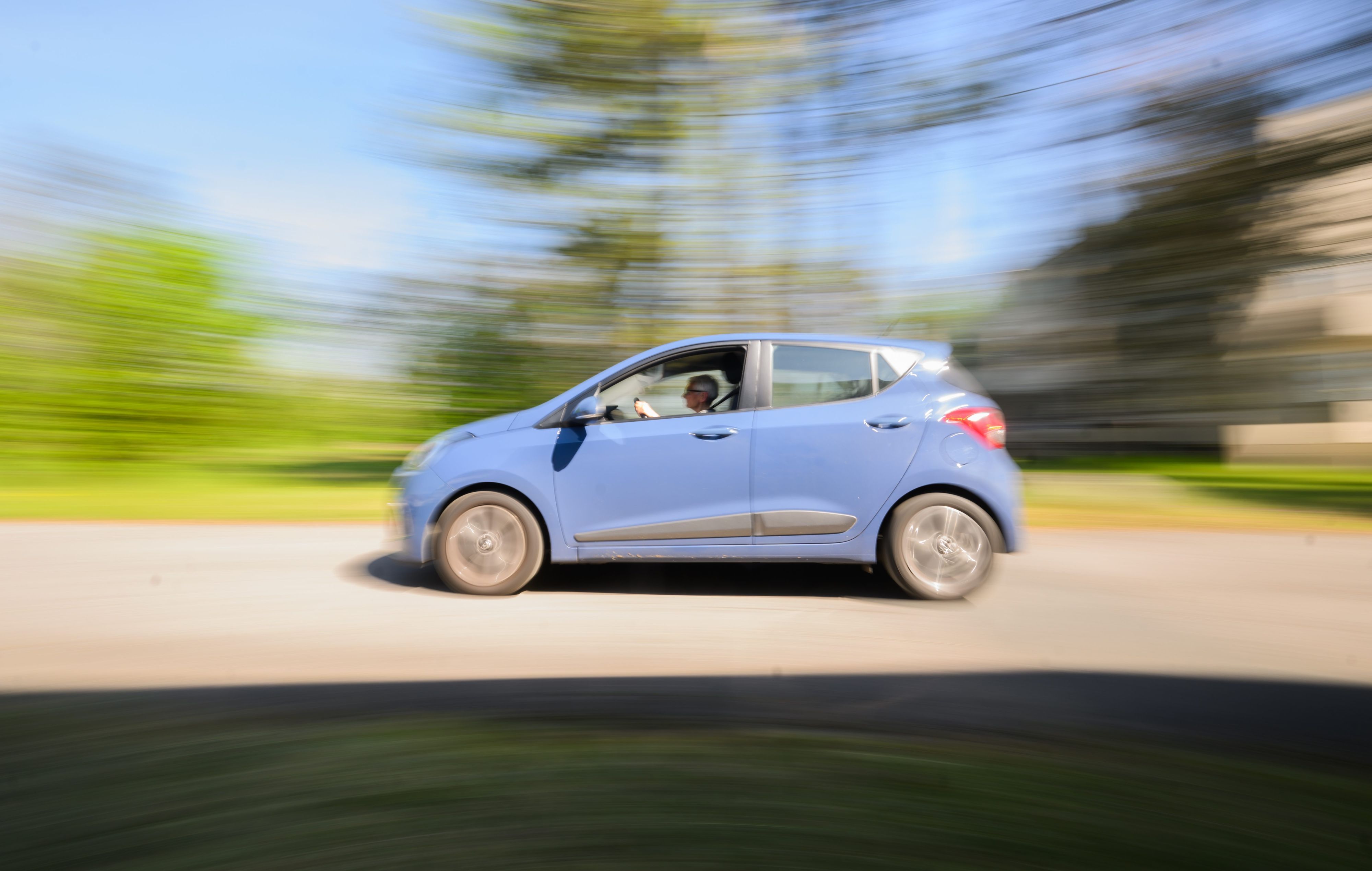 Ein blaues Auto fährt auf einer Straße, im Hintergrund sind verwaschen Bäume und ene grüne Wiese zu sehen. (Symbolbild)