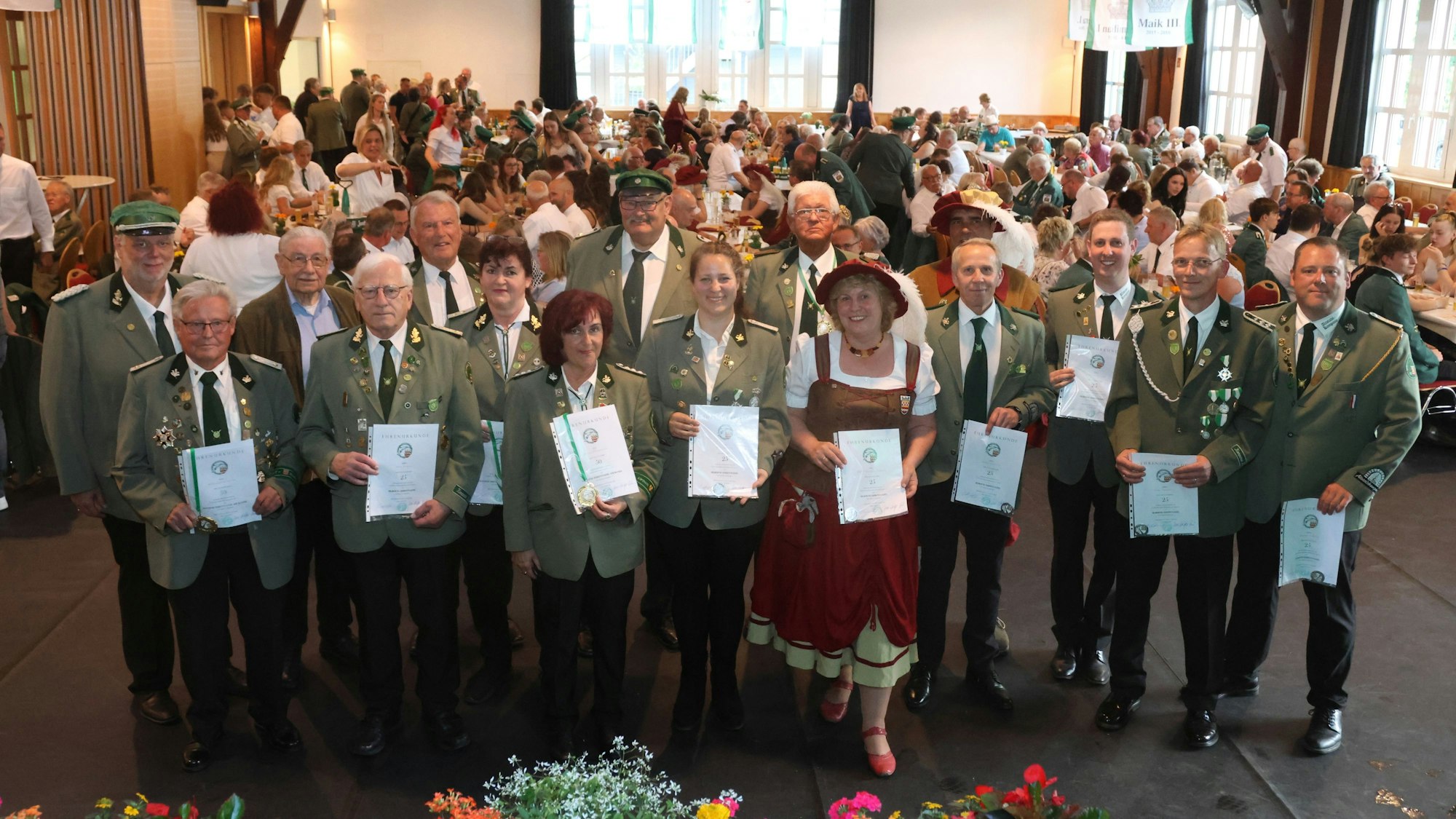 Eine große Gruppe geehrter Schützen steht in einer Festhalle beisammen. In den Händen halten sie Urkunden.