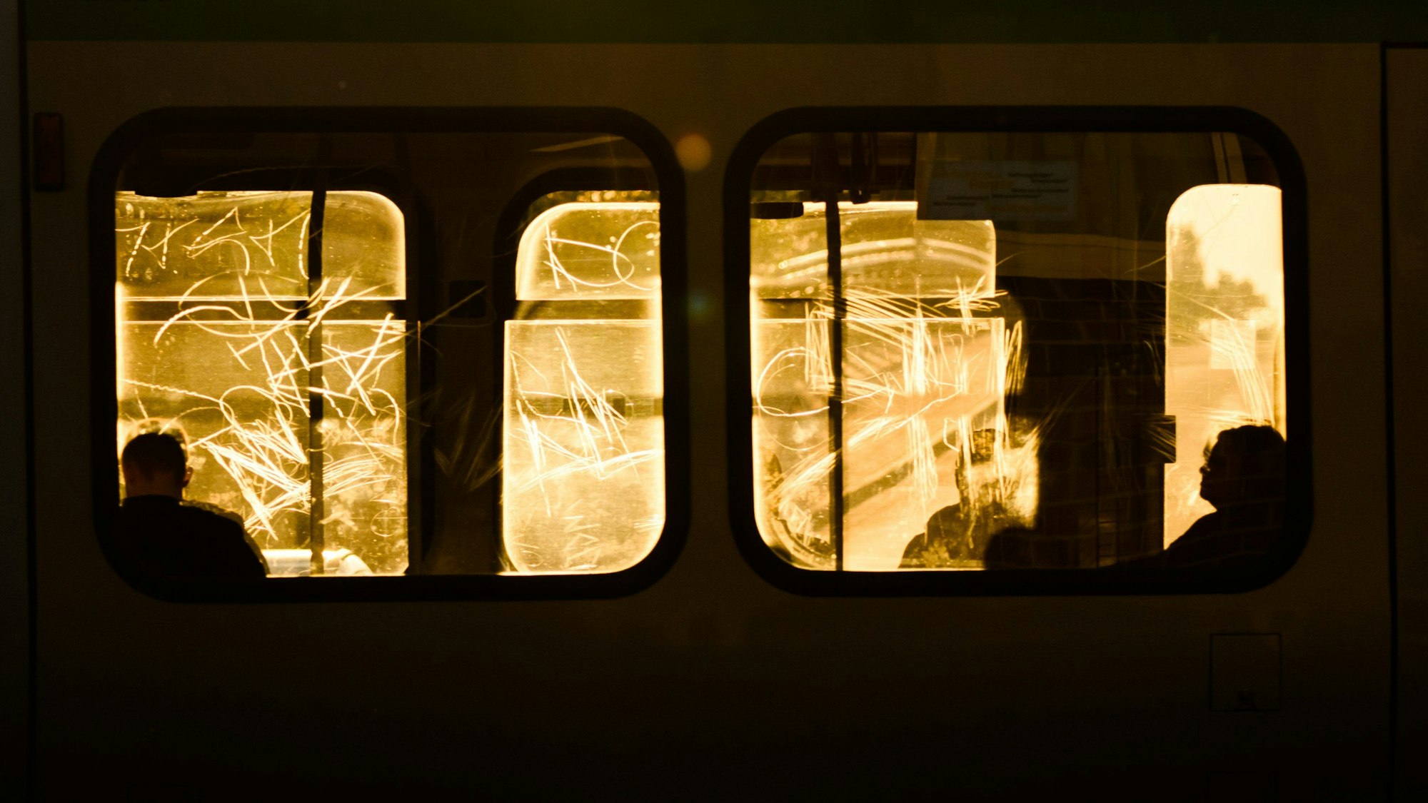 Passanten sitzen am frühen Morgen im Gegenlicht der aufgehenden Sonne in einer Straßenbahn.