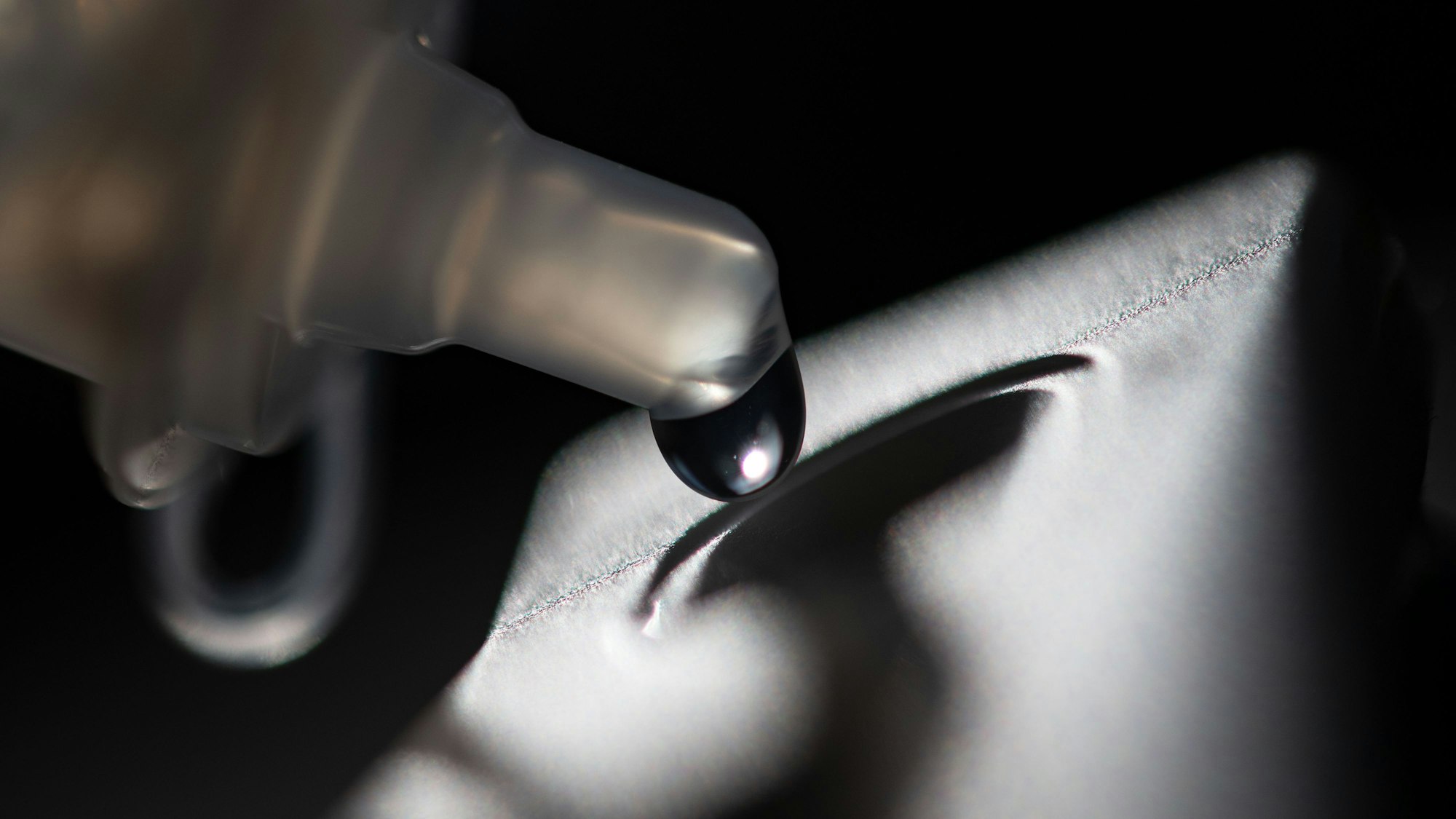 Aus einer Pipette fließt ein Tropfen in Nahaufnahme auf eine Einlassung in einer Fläche.