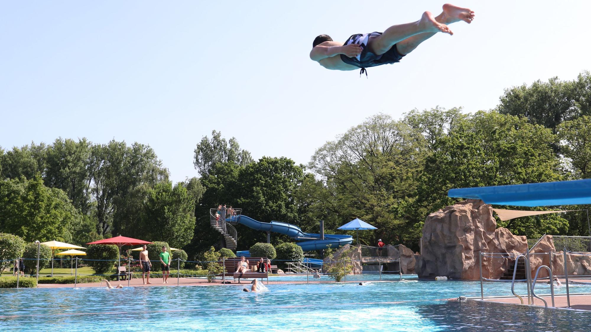 Ein junger Mann springt von einem Sprungbrett ins Freibad-Becken.