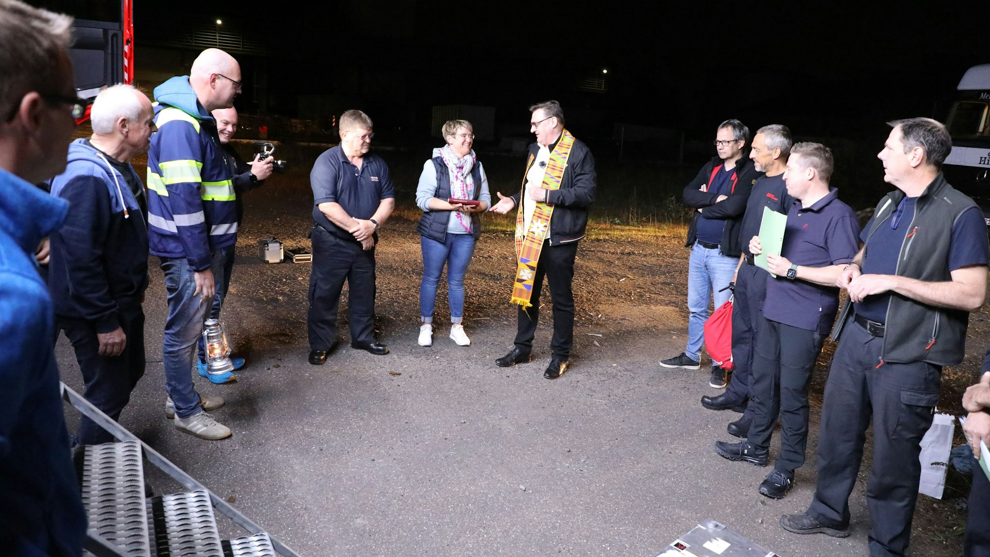 Menschen stehen im Halbkreis neben einem Feuerwehrfahrzeug. Ein Selsorger spricht zu ihnen.