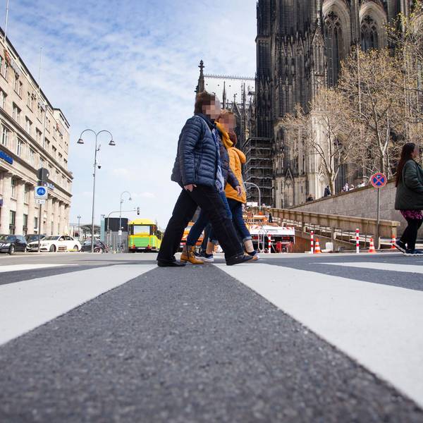 Zwei Menschen queren einen Zebrastreifen nahe des Domes.