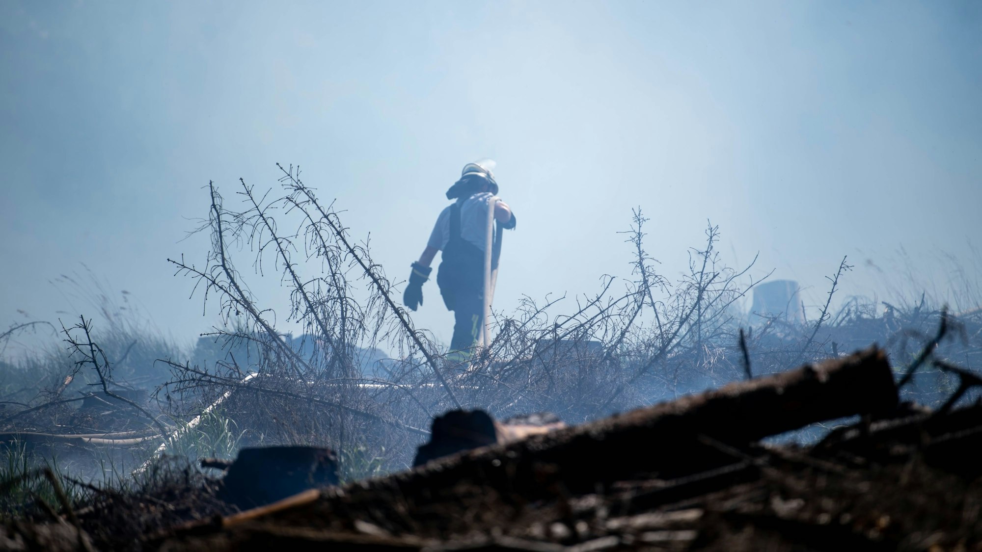 Das Bild zeigt einen Feuerwehrmann, der sich durch dichten Rauch und verbranntes Holz kämpft.