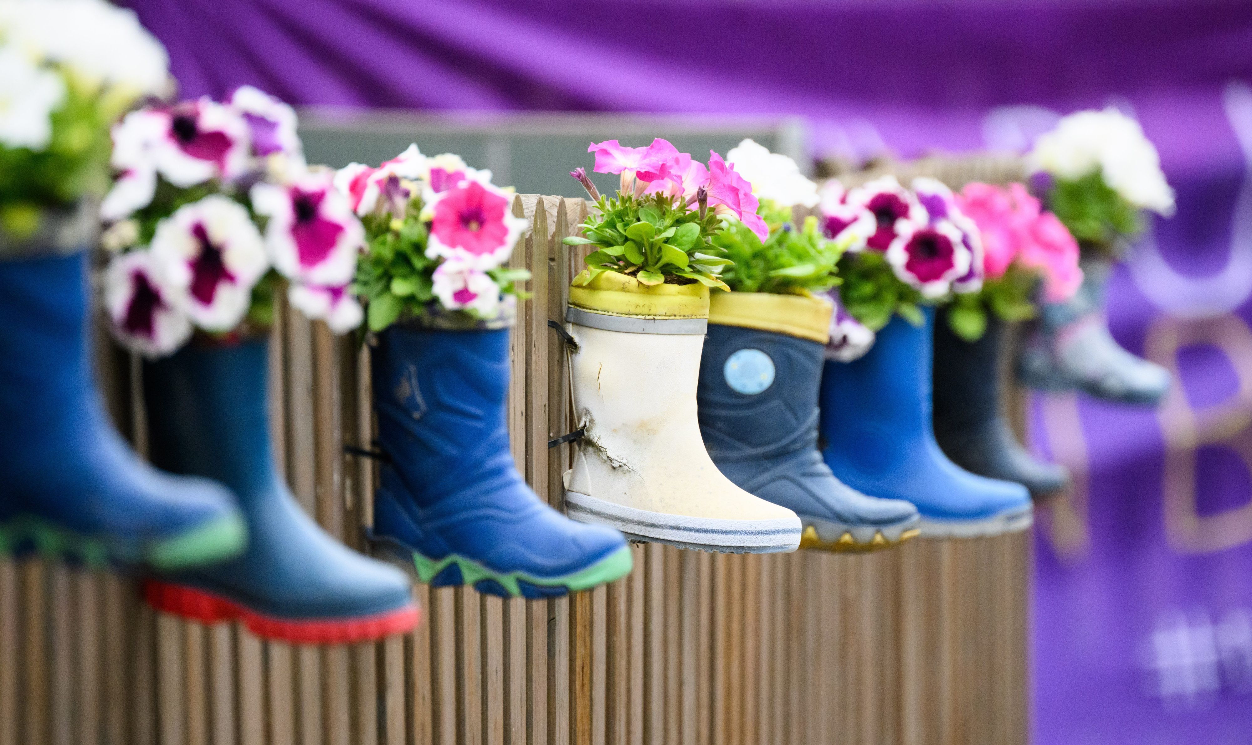 Kinder-Gummistiefel mit Blumen hängen an einem Zaun einer Kindertagesstätte