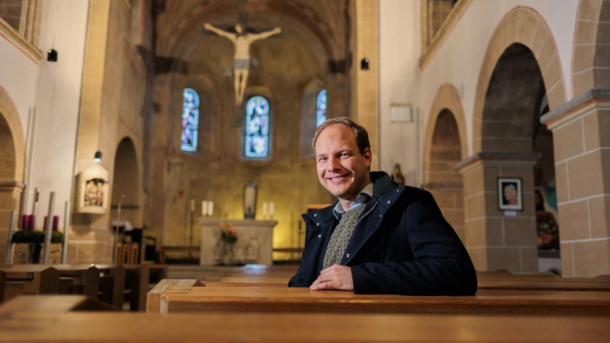 Der Priesteramtsanwärter Sebastian Appolt sitzt auf einer Bank in der Kirche St. Gertrudis und lächelt in die Kamera.