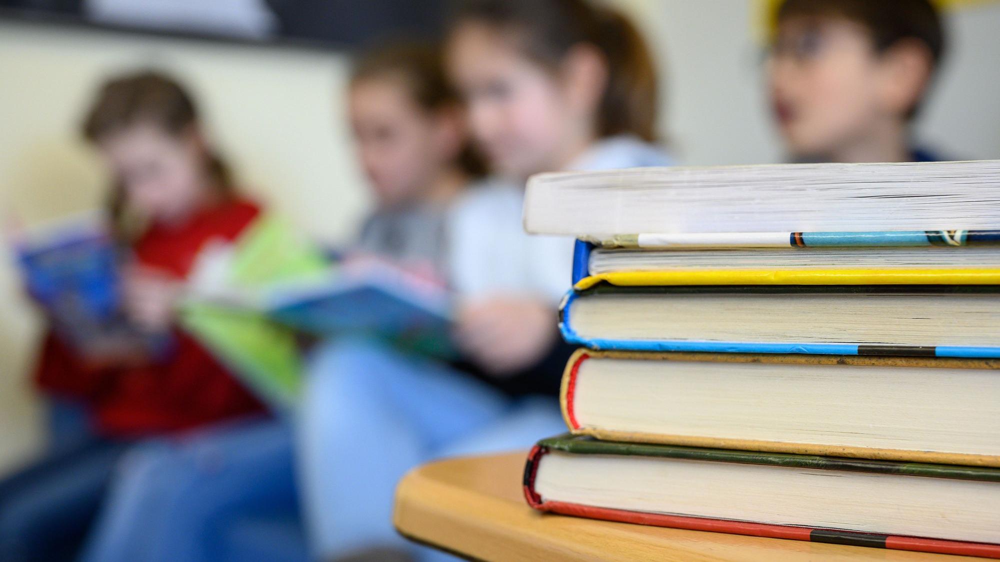 Kinder lesen in einer Grundschule. Im Vordergrund liegt ein Stapel mit Büchern.