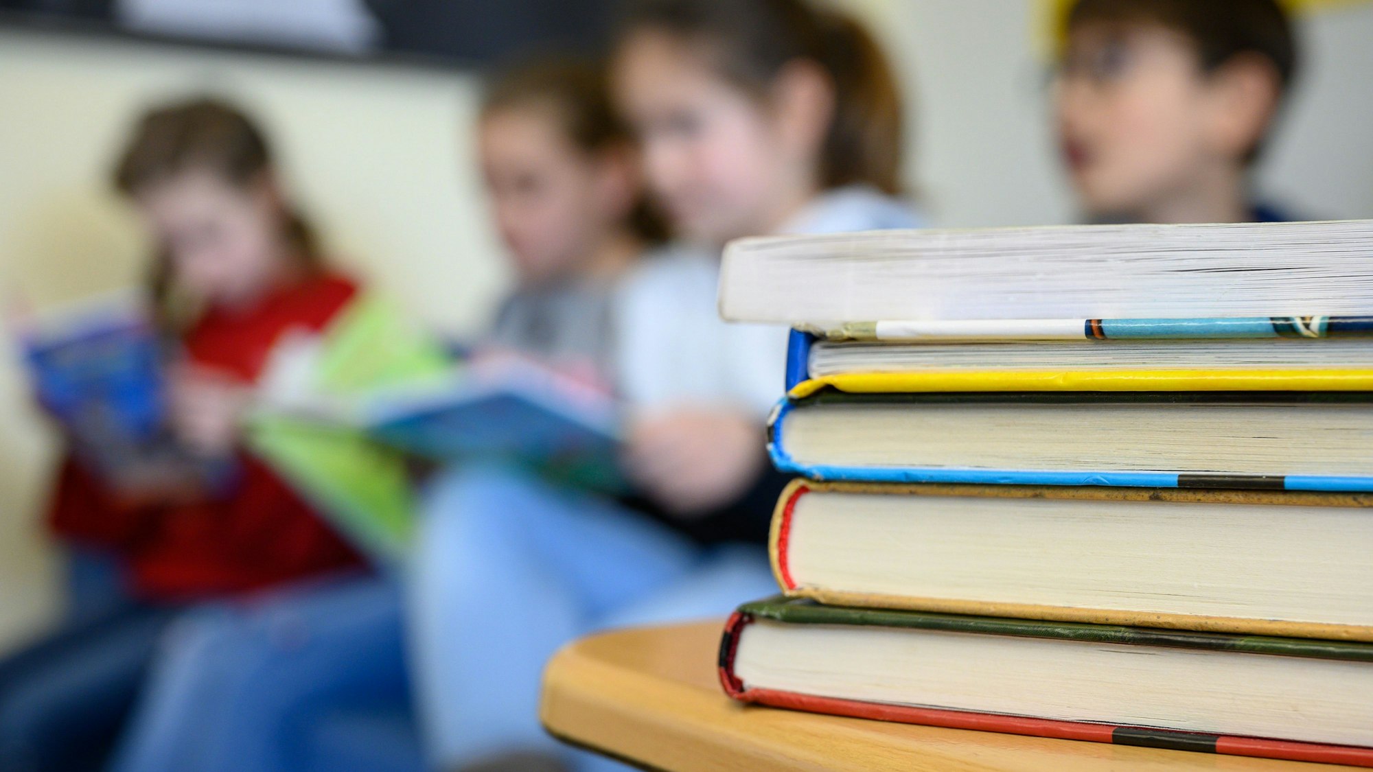 Kinder lesen in einer Grundschule. Im Vordergrund liegt ein Stapel mit Büchern.