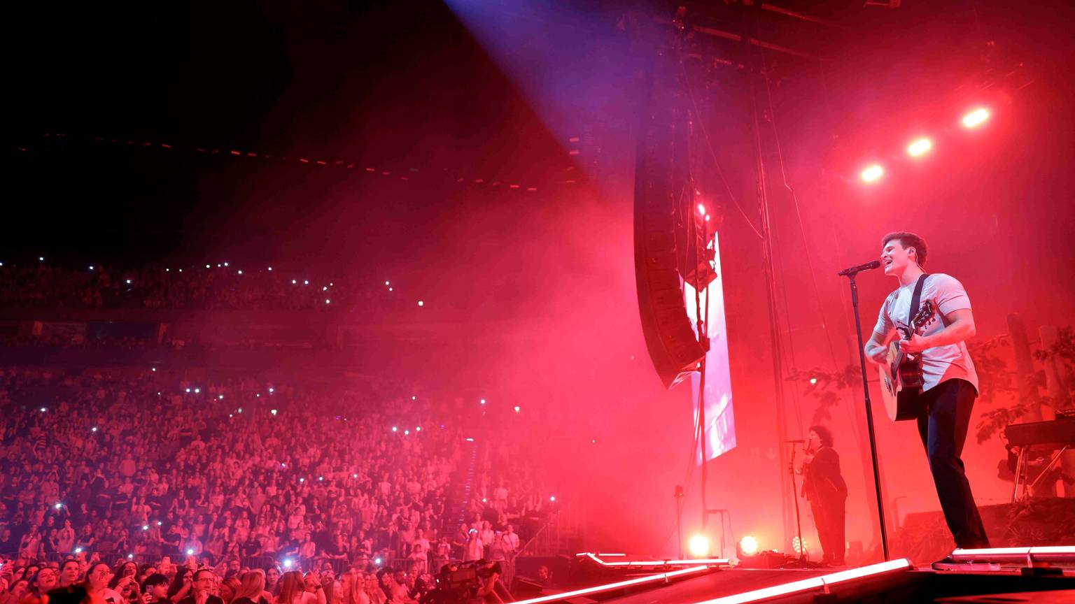 Wincent Weiss spielt auf einer Bühne vor Publikum mit teils leuchtenden Handybildschirmen Gitarre und singt in ein Mikrophon.