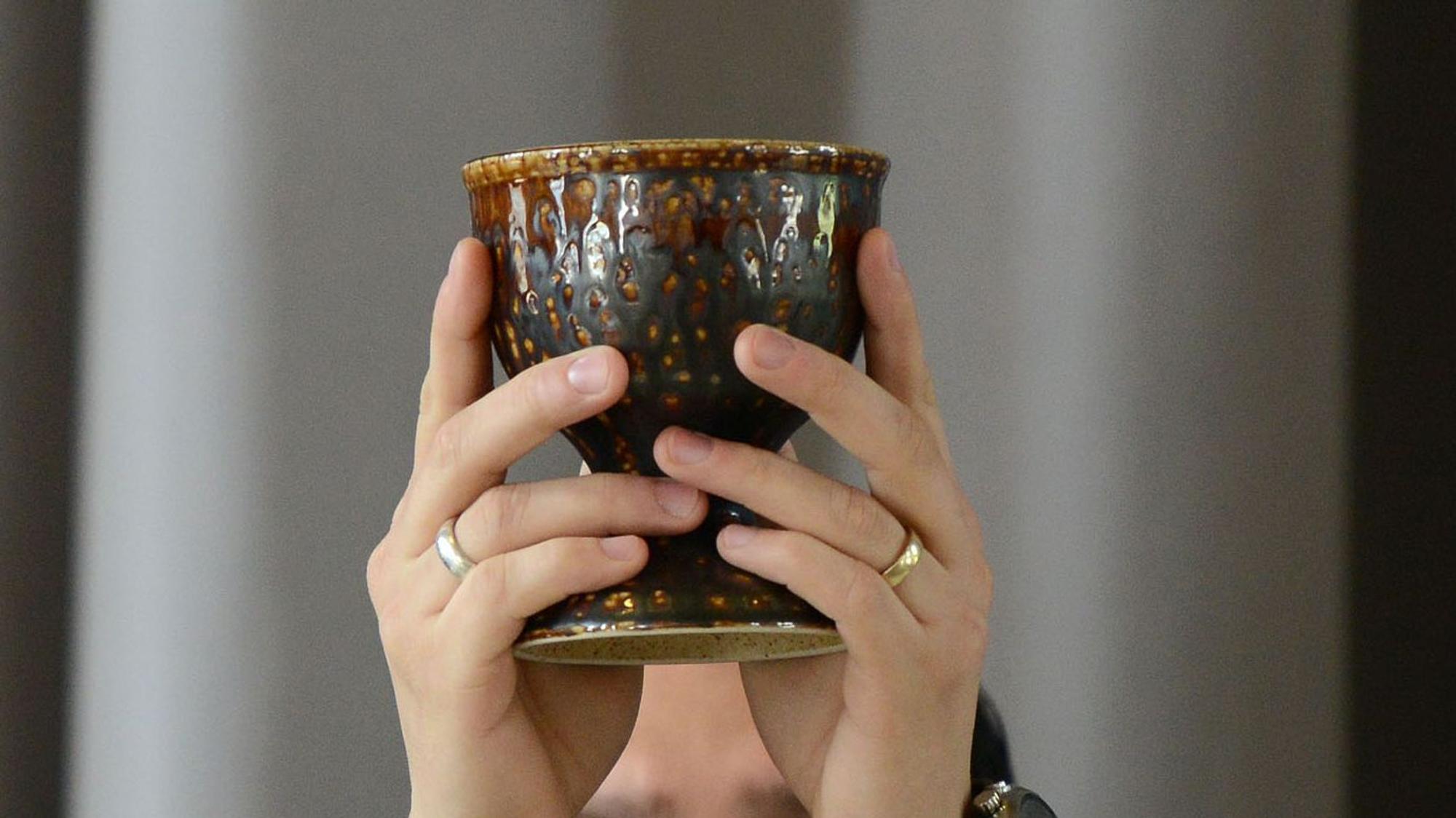 Nahaufnahme auf einen Kelch, den zwei Hände mit Ringen hochheben