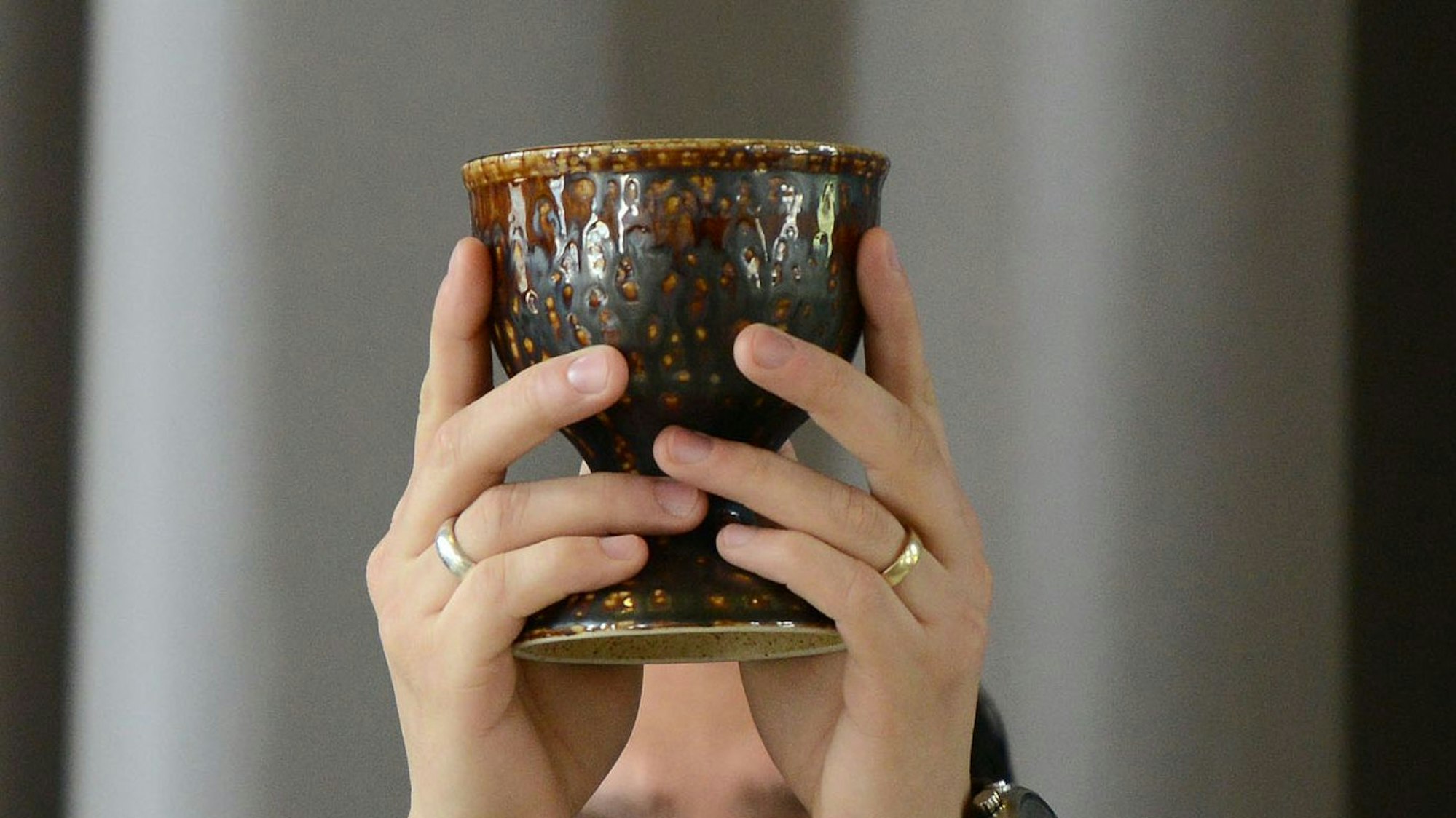 Nahaufnahme auf einen Kelch, den zwei Hände mit Ringen hochheben