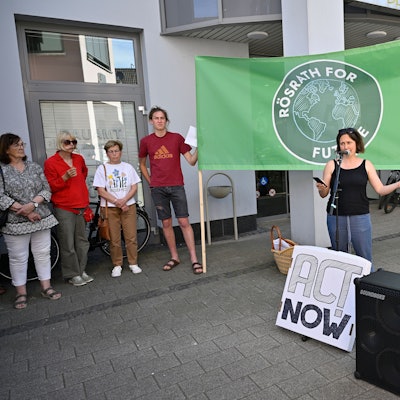 Eine Aktivistin hält eine Rede. Hinter ihr halten zwei Menschen ein Banner mit der Aufschrift „Rösrath for Future“.