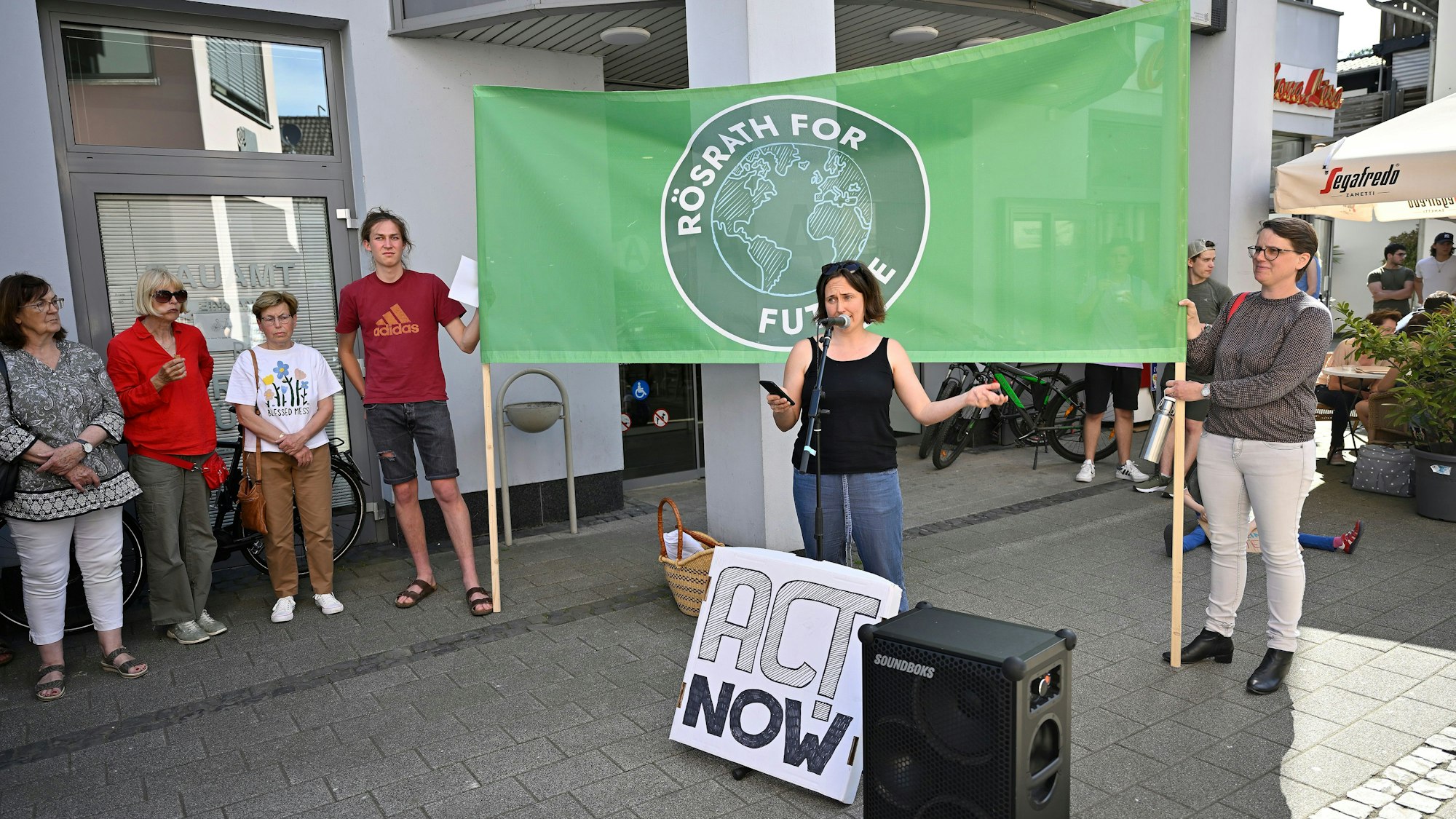 Eine Aktivistin hält eine Rede. Hinter ihr halten zwei Menschen ein Banner mit der Aufschrift „Rösrath for Future“.