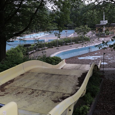 Das Foto zeigt eine Rutsche und dahinter das mit Laub bedeckte Becken des Frechener Freibads.