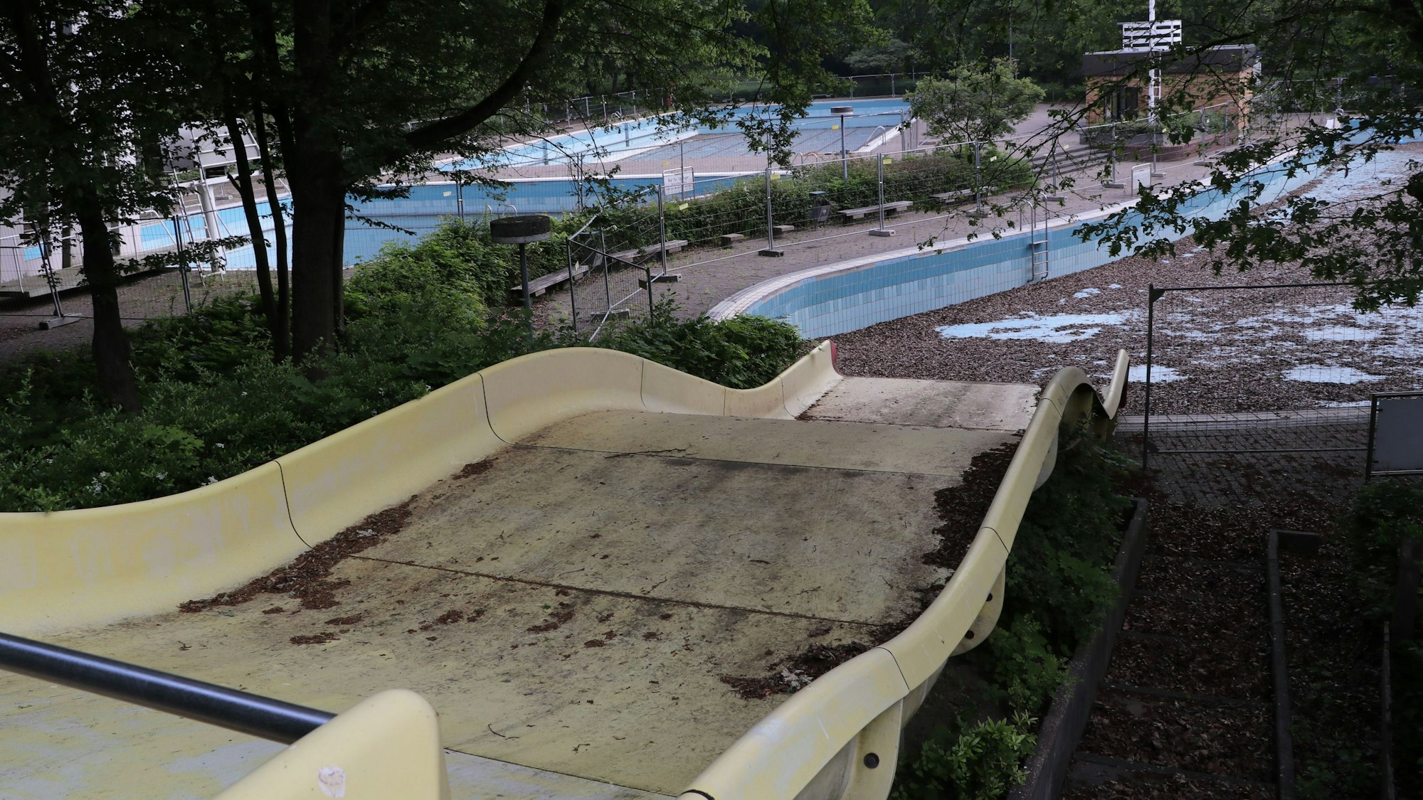 Das Foto zeigt eine Rutsche und dahinter das mit Laub bedeckte Becken des Frechener Freibads.