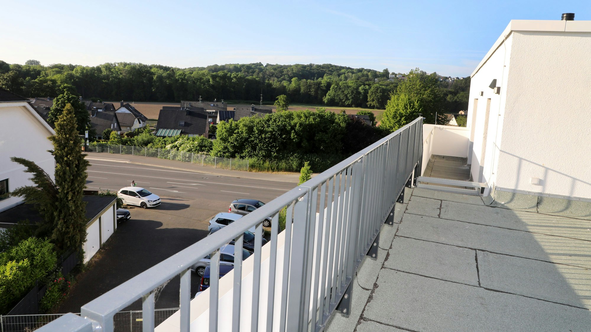 Ein von einem Geländer umgebenes Flachdach liegt im Vordergrund, im Hintergrund ist der Blick über einen Ort, Wiesen und Wälder zu sehen.
