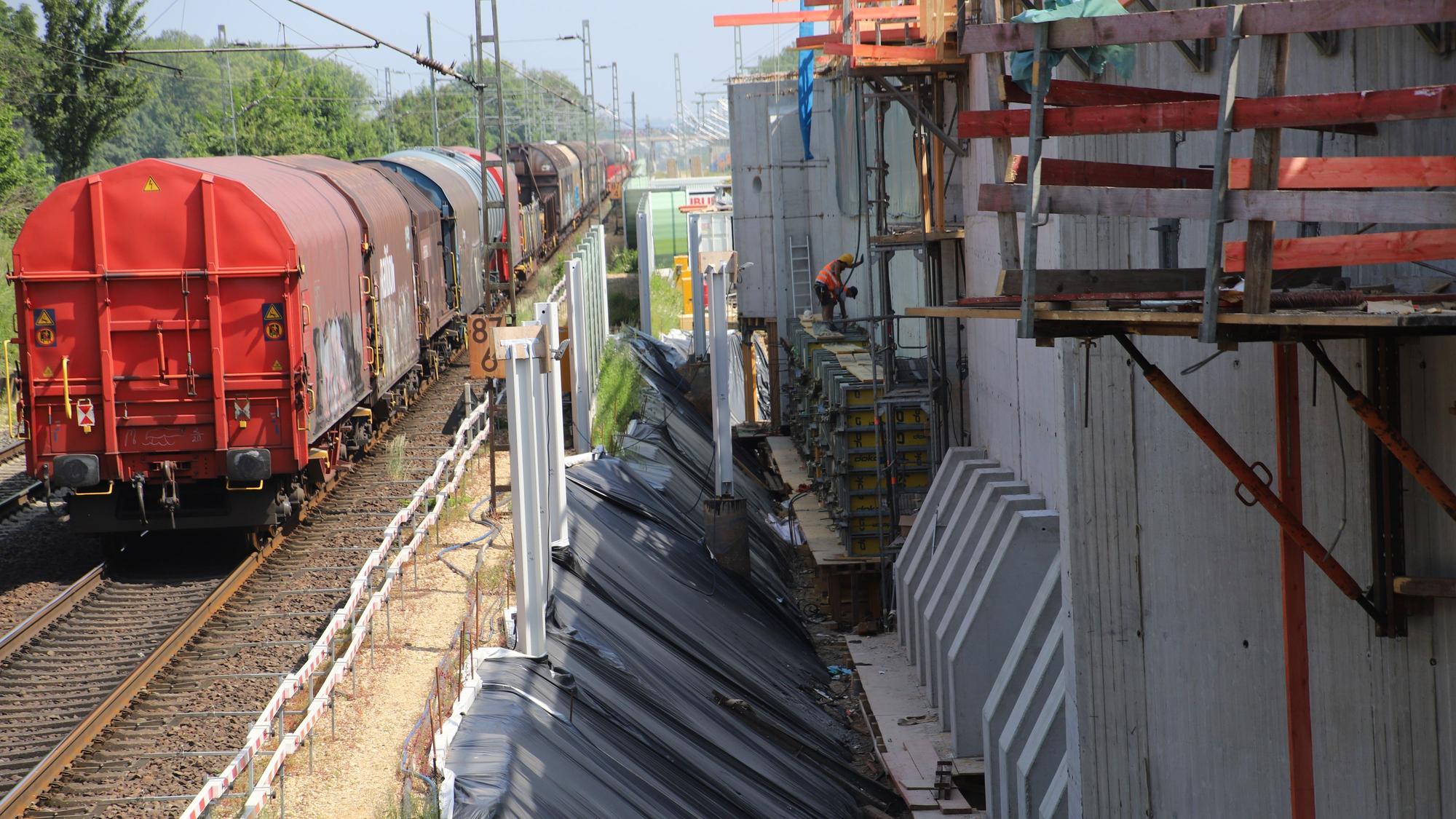 Ein Güterzug steht auf den Schienen neben einer großen Baustelle.
