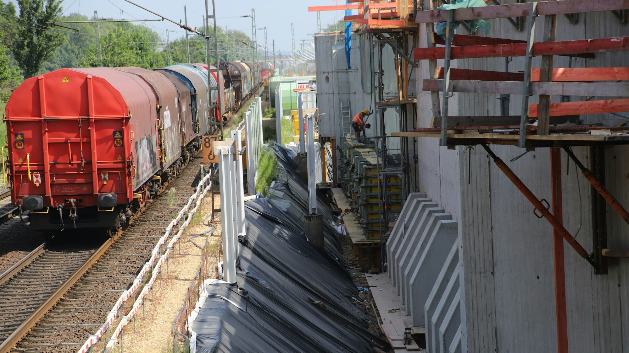 Ein Güterzug steht auf den Schienen neben einer großen Baustelle.