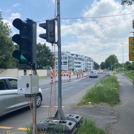 Das Foto zeigt eine Baustellenampel und eine verengte Fahrspur: Die Arbeiten zur Errichtung des neuen Kreisverkehrs an Alte-Bonnstraße und Otto-Wels-Straße werden länger dauern, als ursprünglich geplant.
