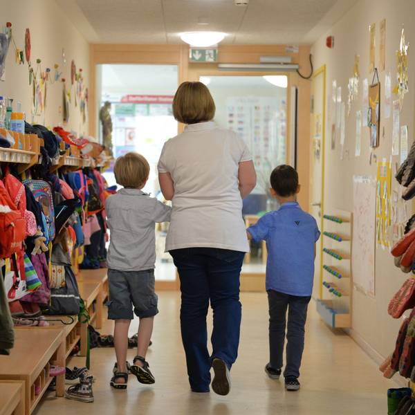 Eine Erzieherin geht mit zwei Kindern über den Flur einer Kita.