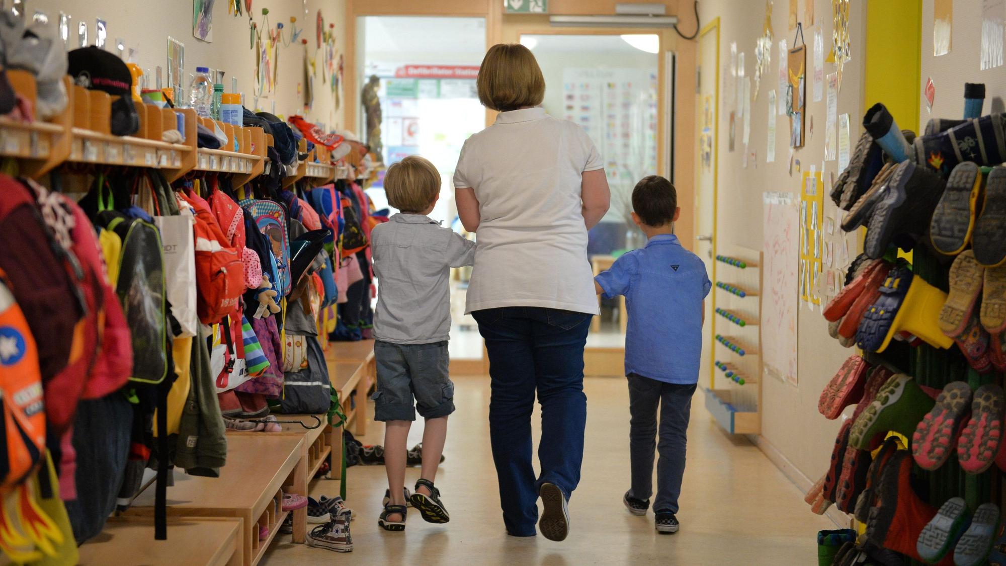 Eine Erzieherin geht mit zwei Kindern über den Flur einer Kita.