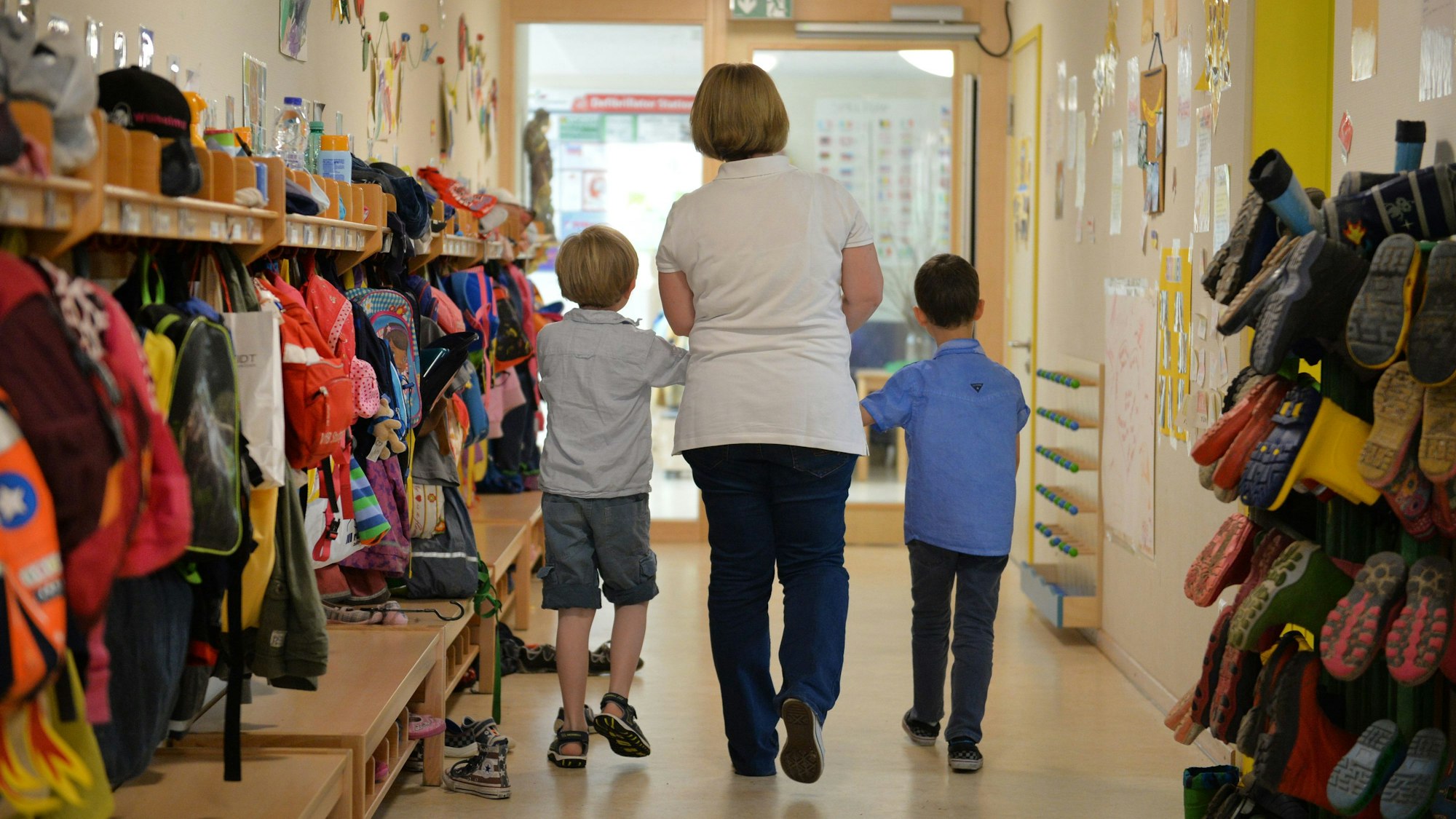 Eine Erzieherin geht mit zwei Kindern über den Flur einer Kita.
