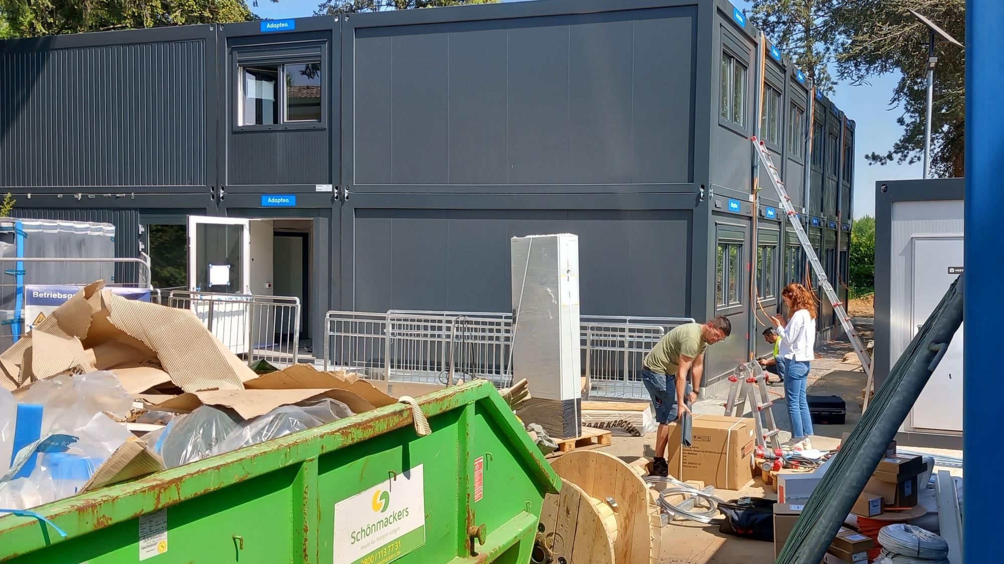 Neben Containern arbeiten drei Personen.