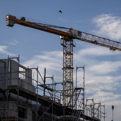 Ein Turmdrehkran ragt in den Himmel auf einer Baustelle zwischen neu errichteten Wohnhäusern. Der Wohnungsbau in Köln stagniert seit Jahren auf niedrigem Niveau. (Symbolbild)