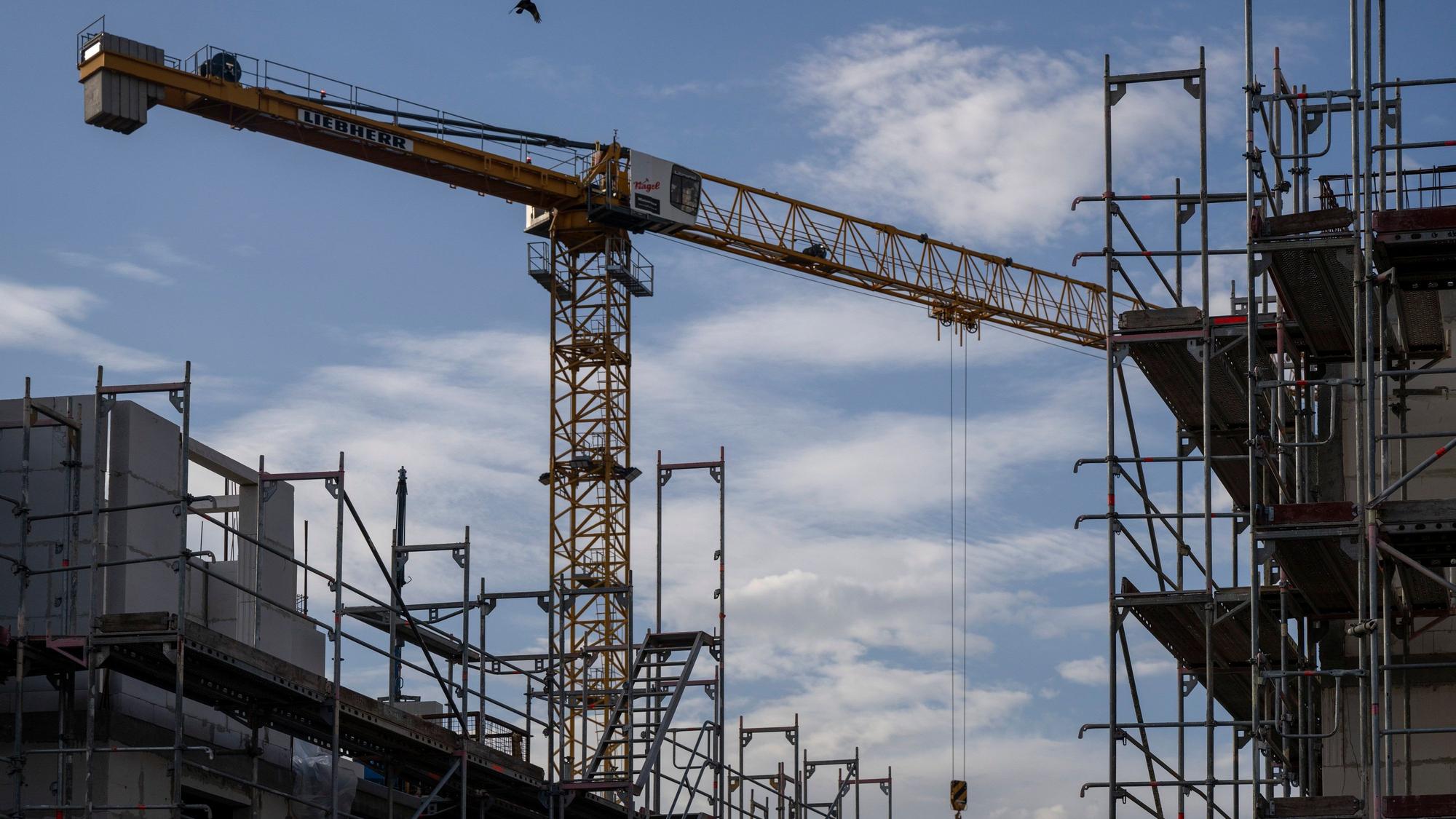 Ein Turmdrehkran ragt in den Himmel auf einer Baustelle zwischen neu errichteten Wohnhäusern. Der Wohnungsbau in Köln stagniert seit Jahren auf niedrigem Niveau. (Symbolbild)