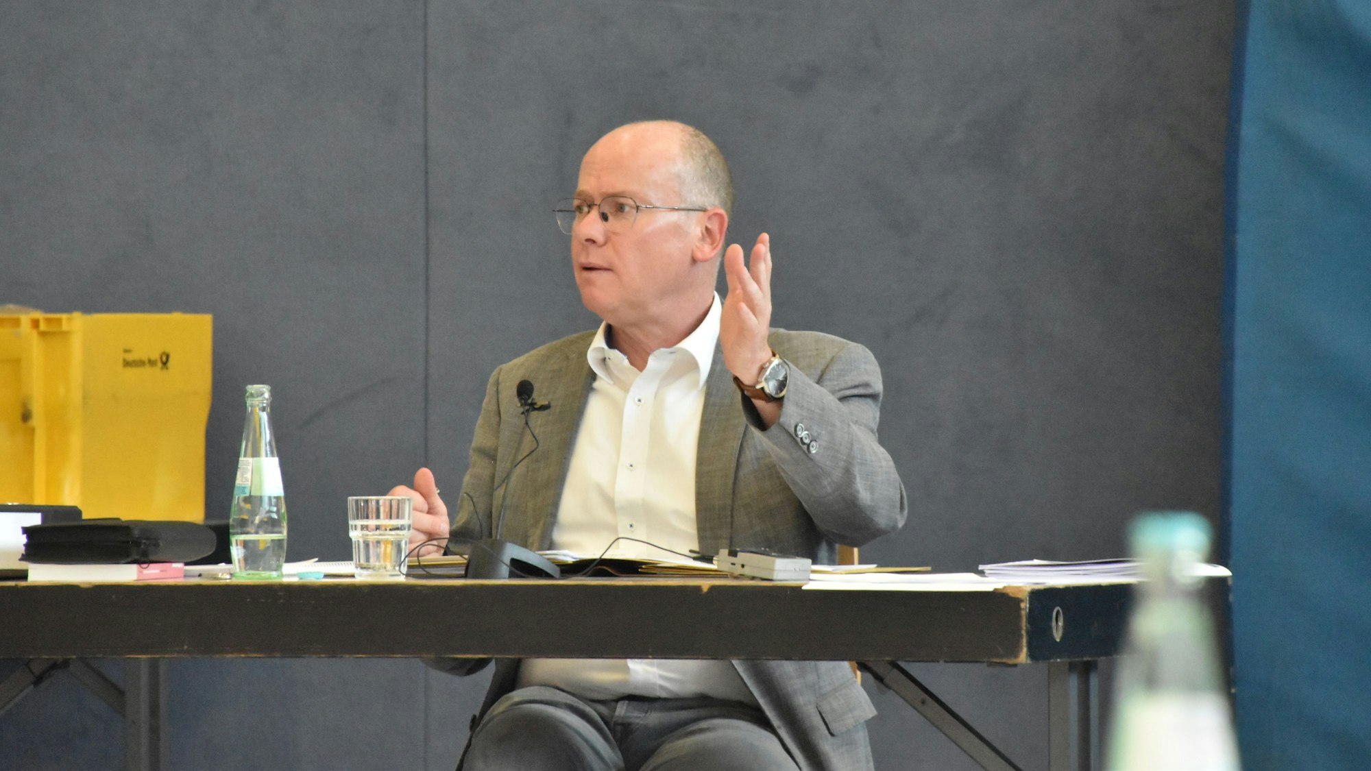 Bürgermeister Mario Loskill gestikuliert mit erhobener Hand und sitzt an einem Schreibtisch in einer Sporthalle.