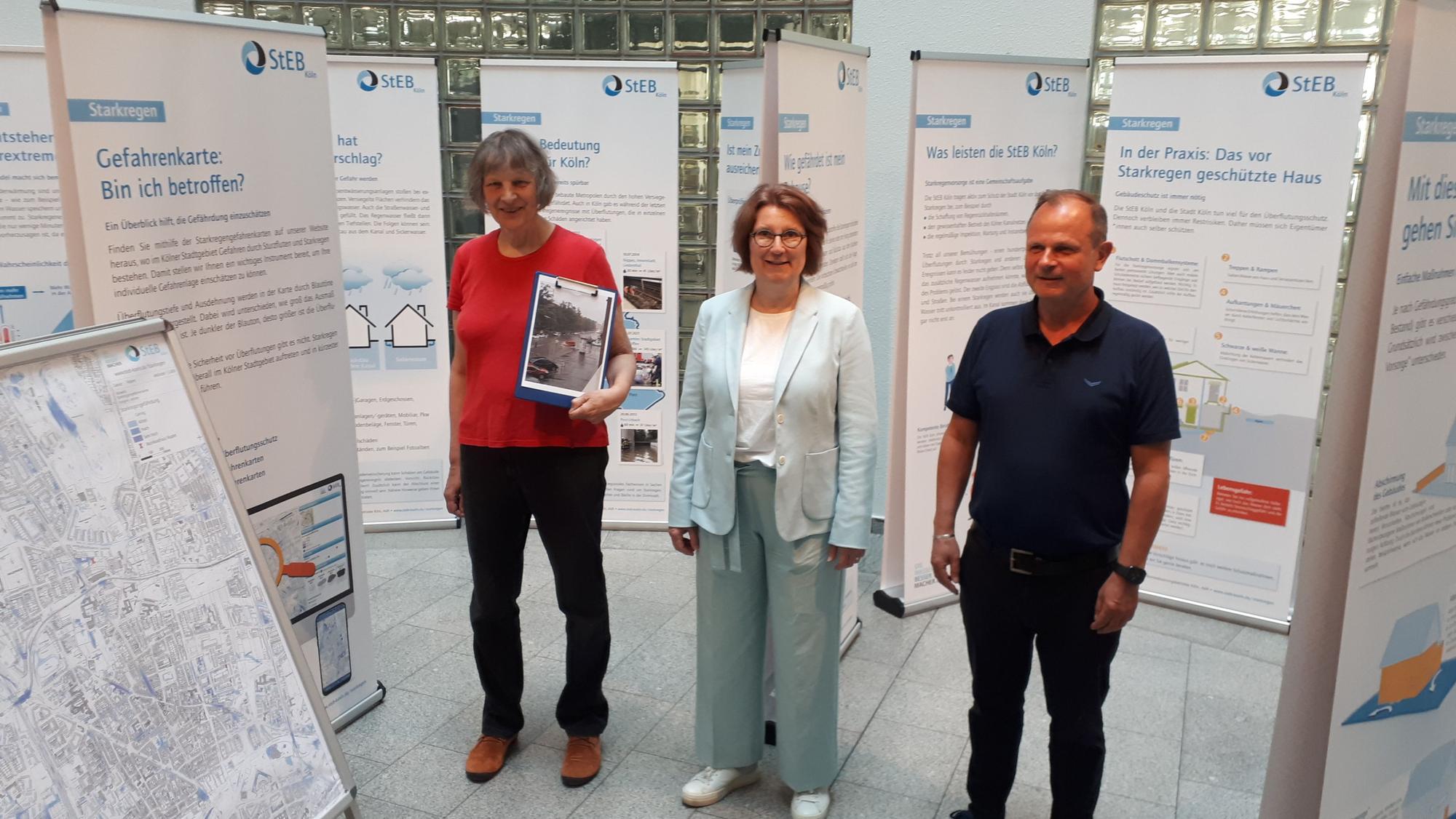 Zwei Frauen und ein Mann stehen zwischen Ausstellungstafeln im Foyer des Rathauses von Nippes.