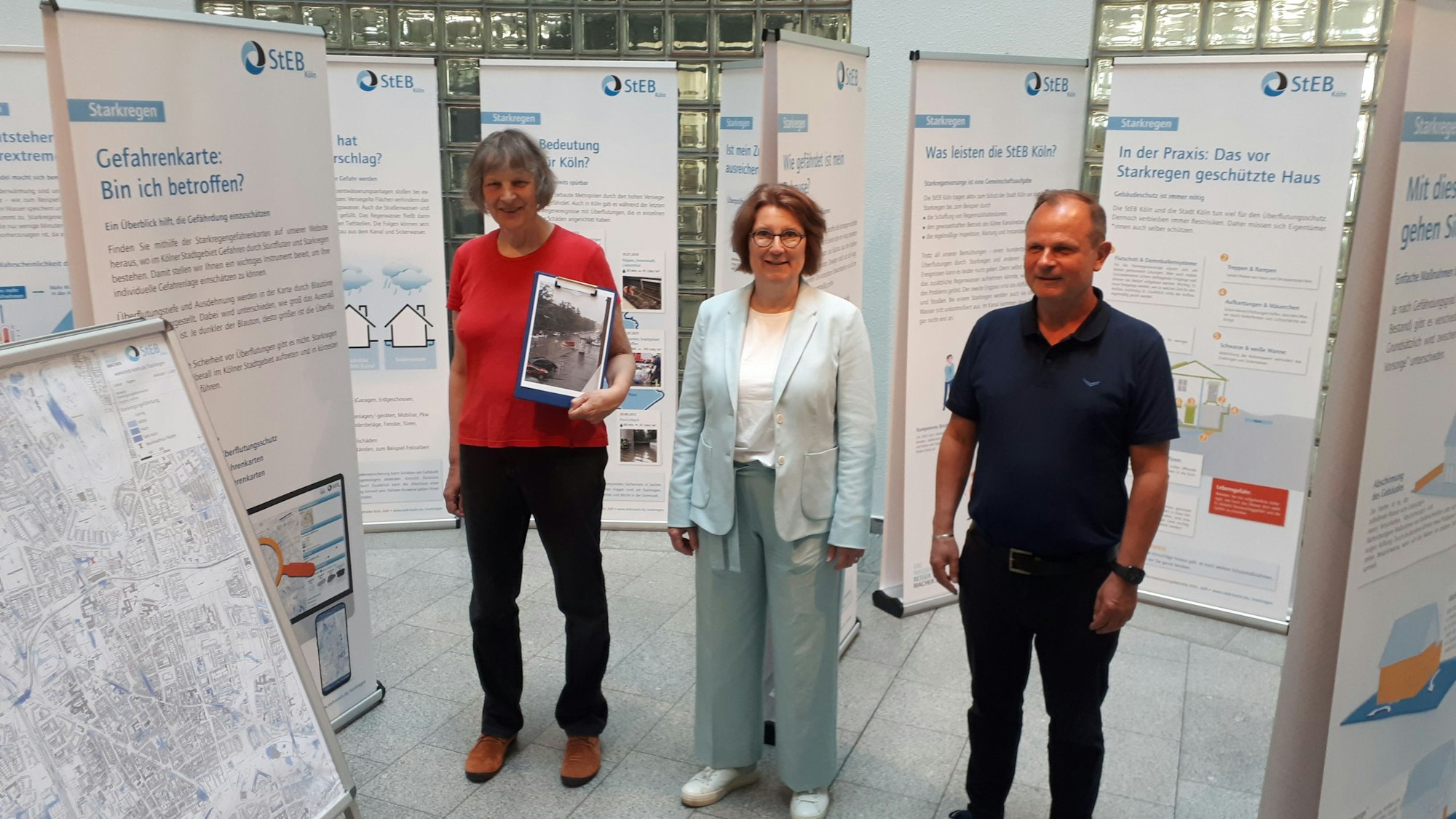 Zwei Frauen und ein Mann stehen zwischen Ausstellungstafeln im Foyer des Rathauses von Nippes.