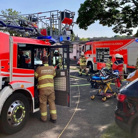 Feuerwehrfahrzeuge stehen auf der Straße, Schlauchleitungen sind ausgerollt, Tragen und Rettungsdienstmitarbeiter stehen bereit.