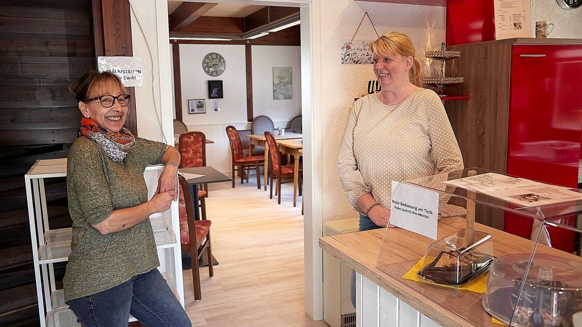 Das Bild zeigt zwei Frauen, die in einem Café an einem Regal und einer Theke stehen.